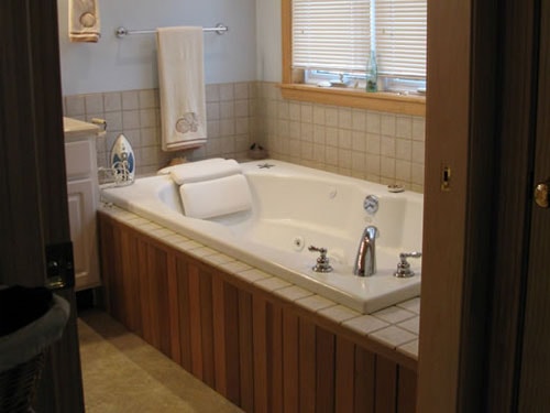 Bathroom with jetted soaking tub, tile surround, and wood panel skirt