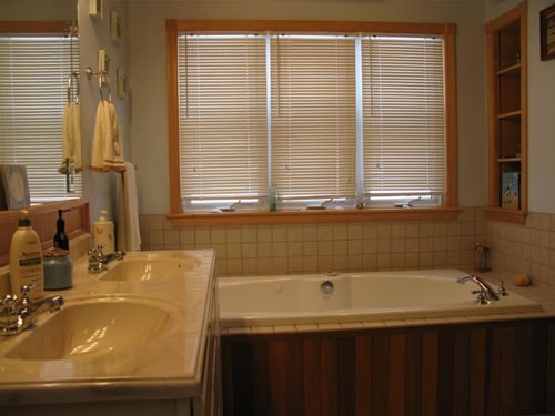 Bathroom with double sink vanity, tile surround jetted tub, and wood blinds