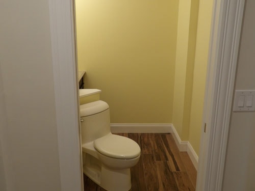 Renovated half bath with yellow walls, wood-look tile floor, and new toilet