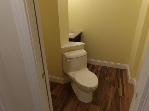 Half bath with yellow walls, wood-look tile floor, and corner shelf