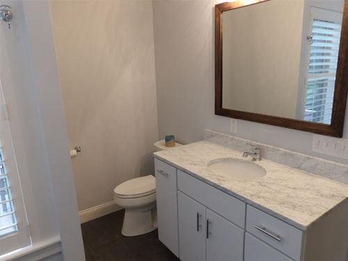 Renovated bathroom with white vanity, marble countertop, and wood-framed mirror
