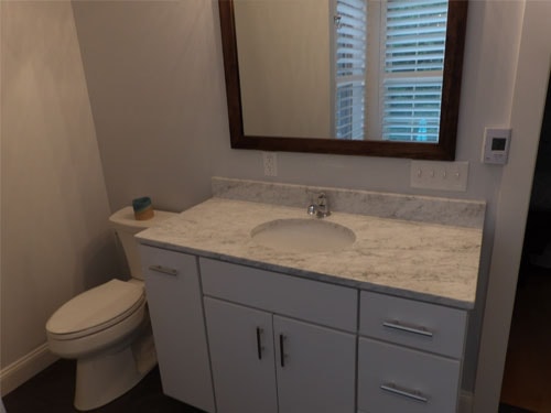 Completed bathroom remodel with white vanity, marble countertop, and wood-framed mirror