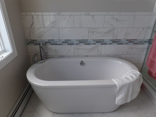 Freestanding soaking tub with marble tile surround and decorative glass mosaic border