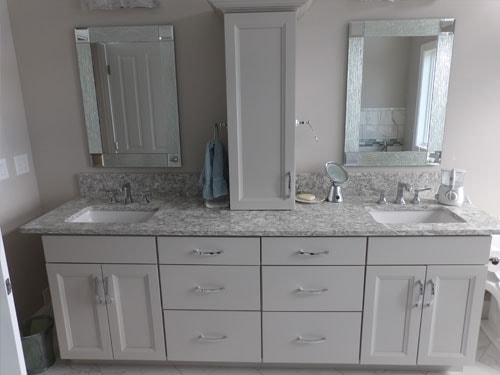 Double vanity with gray cabinets, granite countertop, center tower cabinet, and beveled mirrors