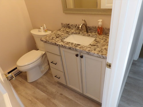 Half bath with white vanity, granite countertop, and wood-look luxury vinyl plank floor