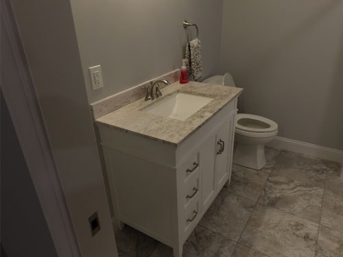 Bathroom vanity with white cabinets, granite countertop, and large format tile floor
