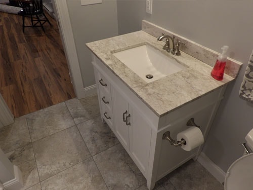 Bathroom vanity with white cabinets, granite countertop, and large format tile floor