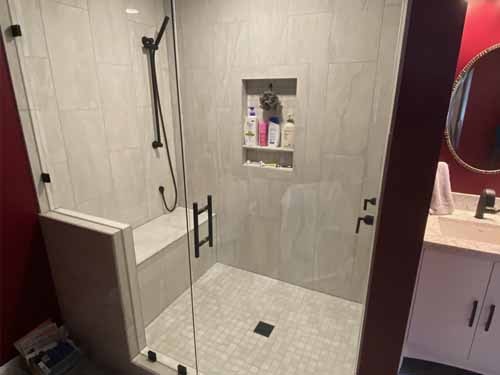 Custom tile shower with large format gray tile, built-in niche, bench seat, and frameless glass door