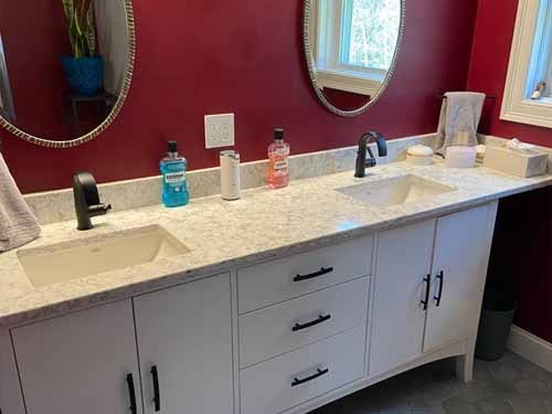 Double vanity remodel with white cabinets, marble countertop, oval mirrors, and burgundy accent wall