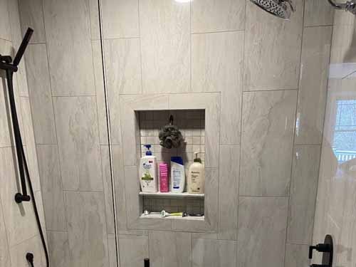 Custom tile shower niche with large format gray tile, built-in shelf, and rain shower head