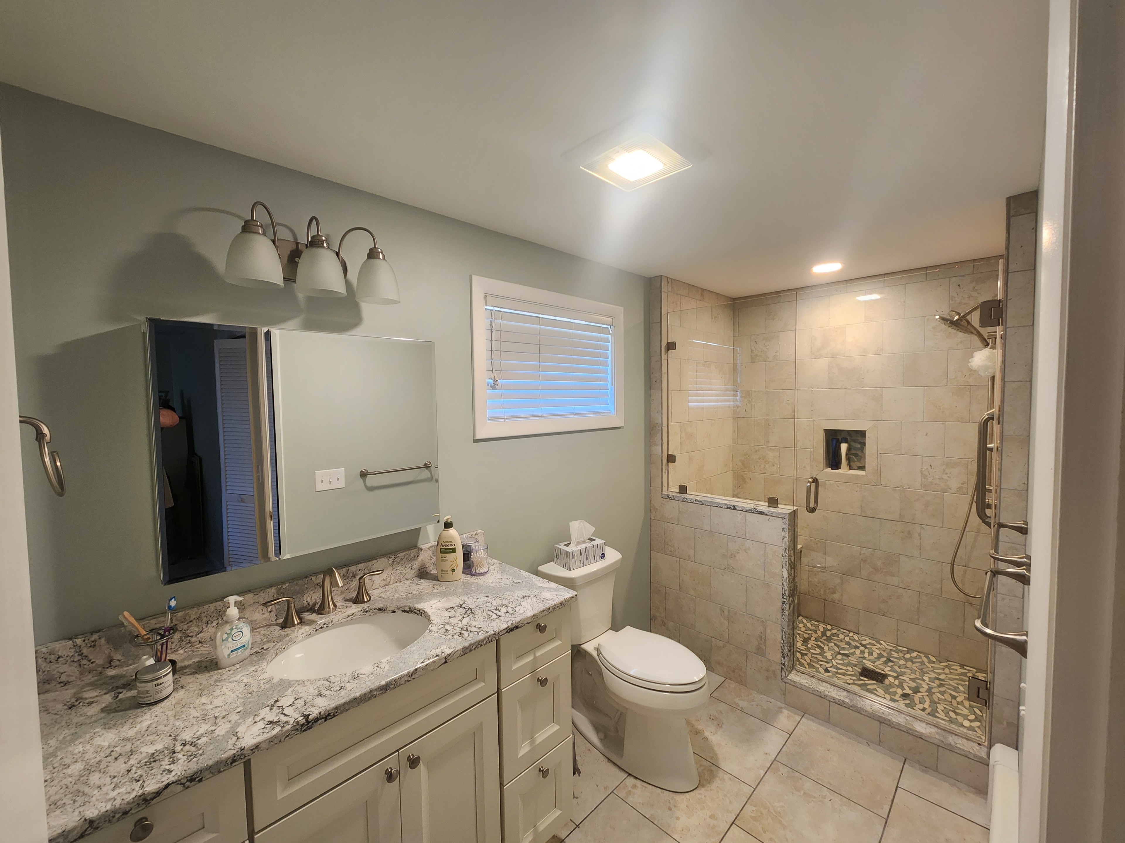 Bathroom remodel with white vanity, granite countertop, tile shower with niche, and pebble floor