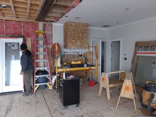 Interior renovation in progress with contractor, ladders, tools, and partially drywalled walls