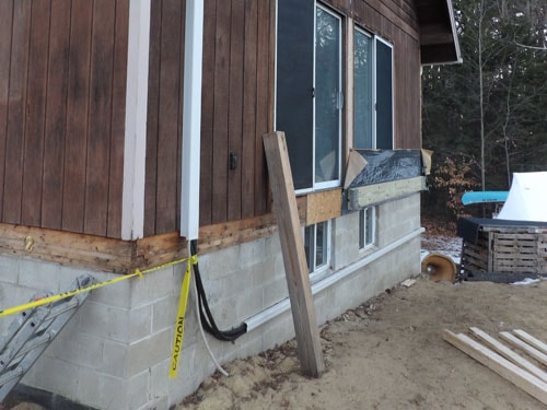 Exterior foundation work with new concrete block, drainage pipe, and caution tape
