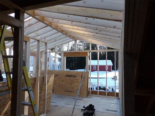 Interior addition framing with vaulted ceiling rafters and large window openings overlooking snowy yard
