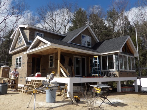 Craftsman home exterior under construction with covered porch framing, cedar shake siding, and deck structure