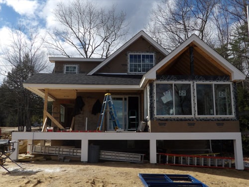Craftsman home exterior nearing completion with covered porch, white deck framing, and cedar shake siding