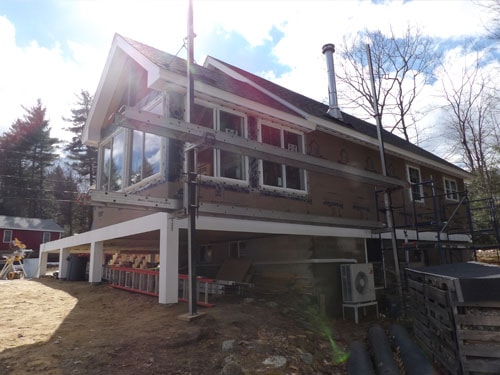 Lakeside home exterior renovation with new white deck structure, large windows, and mini-split installation
