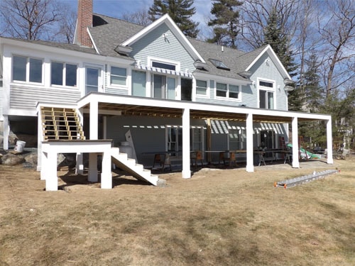 Large lakeside home with expansive white deck and pergola structure under construction