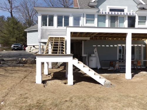 Deck addition under construction with new stair framing, white posts, and covered porch structure