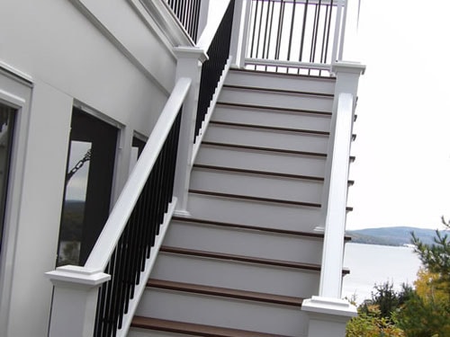 Composite deck staircase with white posts, black balusters, and lake view in background