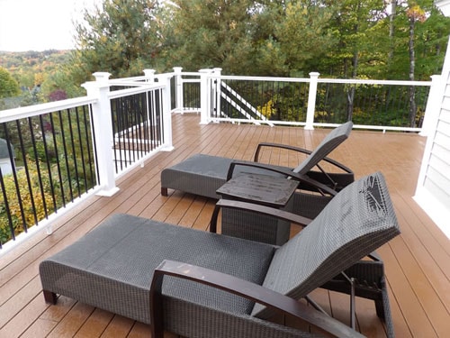Composite deck with chaise lounge chairs, white posts, and black balusters surrounded by trees