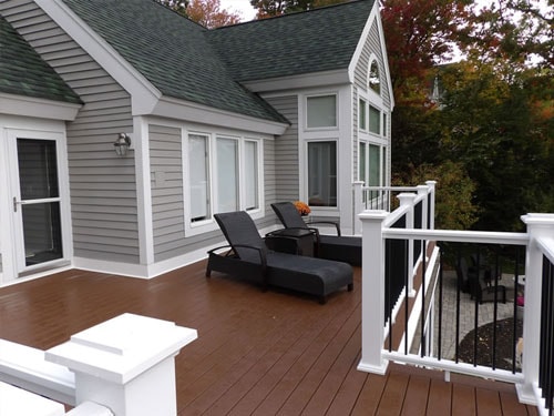 Completed composite deck with chaise lounges, white and black railing, and gray home exterior