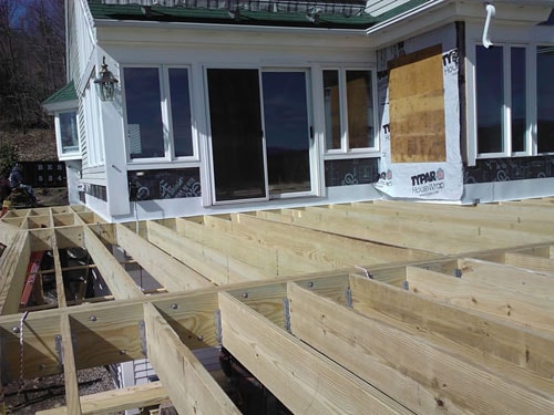 Deck framing in progress with pressure-treated joists and ledger board attached to home