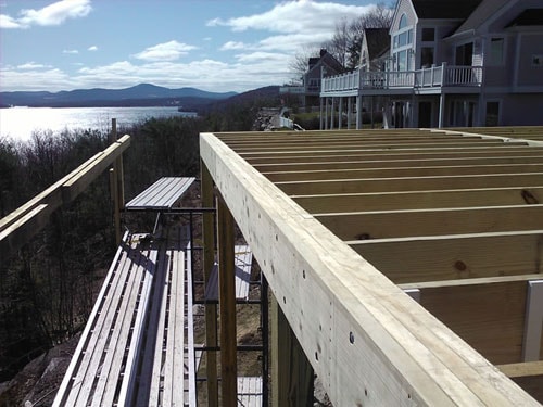 Elevated deck framing with pressure-treated joists overlooking lake and mountain views