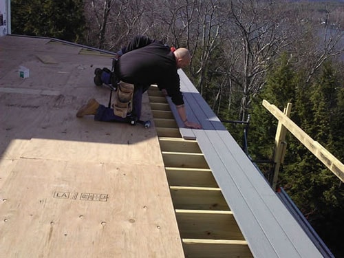 Contractor installing composite deck boards on elevated lakeside deck with lake view