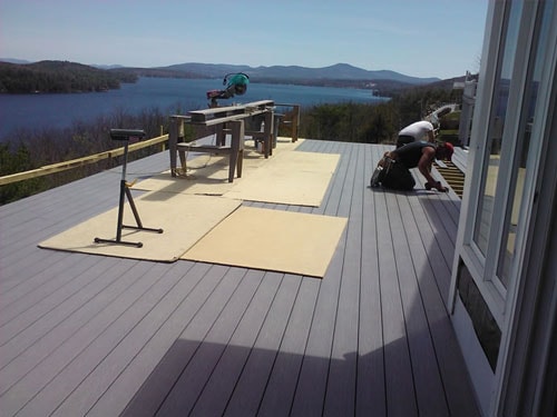 Contractor installing gray composite deck boards on lakeside deck with sweeping lake and mountain views