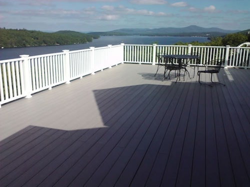 Completed gray composite deck with white railing and black iron furniture overlooking lake and mountains