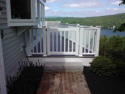 White vinyl deck gate and railing at base of lakeside deck stairs with brick patio and lavender plantings