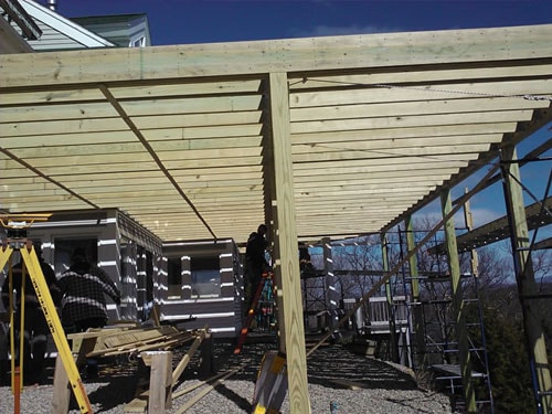 Pergola framing under construction with pressure-treated posts and rafters over lakeside home