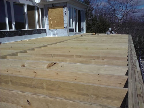 Deck framing with pressure-treated joists and ledger board attached to lakeside home exterior