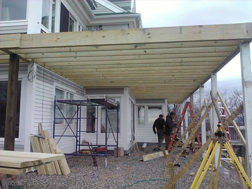 Large deck framing with pressure-treated posts and joists, crew working below on lakeside home