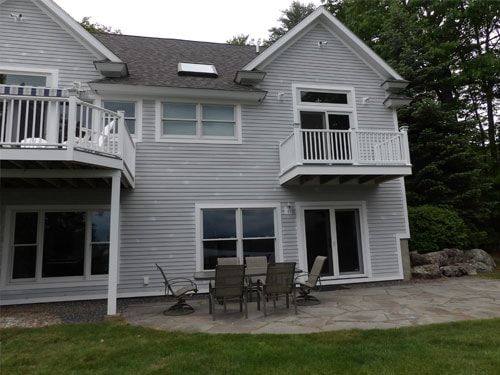Completed lakeside home exterior with flagstone patio, multiple decks, and balcony overlooking water