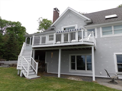 Lakeside home exterior with elevated white deck, curved staircase, white railings, and balcony