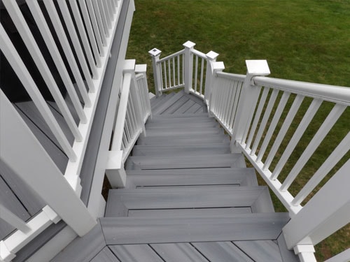 Looking down gray composite deck stairs with white vinyl railings, solar post caps, and lawn below