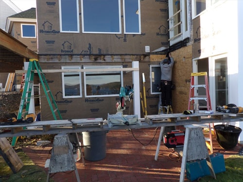 Contractor installing exterior trim and windows on lakeside home with HydroGap weather barrier and scaffolding
