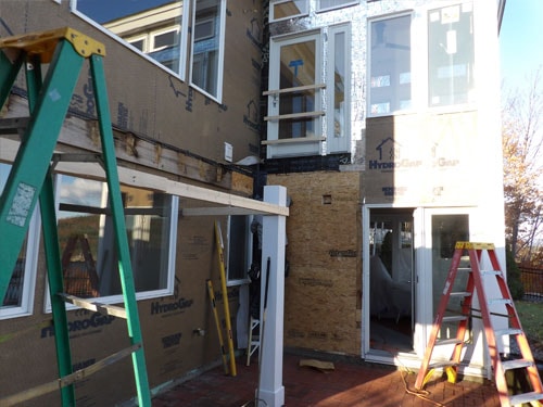 Exterior window and trim installation in progress on lakeside home with HydroGap wrap and ladders