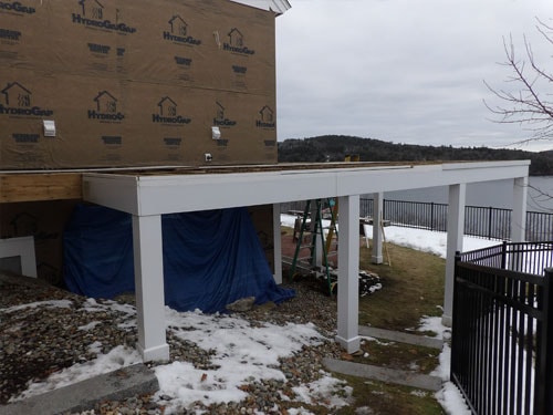 Pergola structure under construction with white posts and flat roof framing, lakeside home in winter