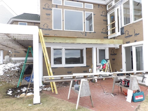 Pergola ledger beam and post framing in progress on lakeside home exterior with Makita tools on sawhorse