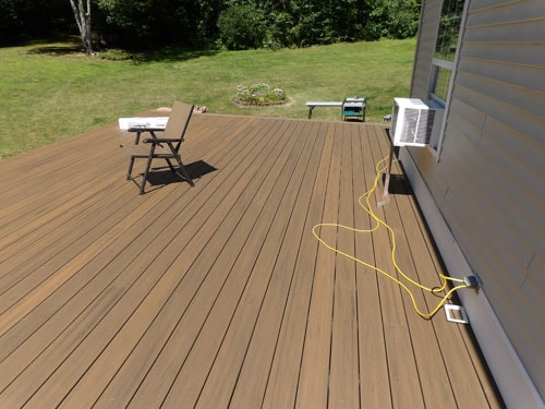Newly completed brown TimberTech composite deck with lounge chair and mini-split unit on gray home exterior