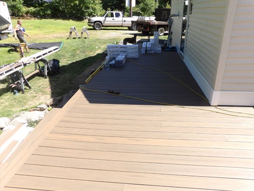 Two-tone composite deck installation in progress with tan and gray boards, contractor and truck in background