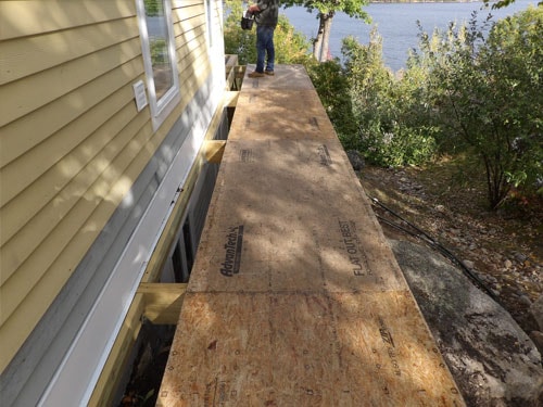 Contractor standing on new deck subfloor framing with AdvanTech sheathing, lakeside yellow home