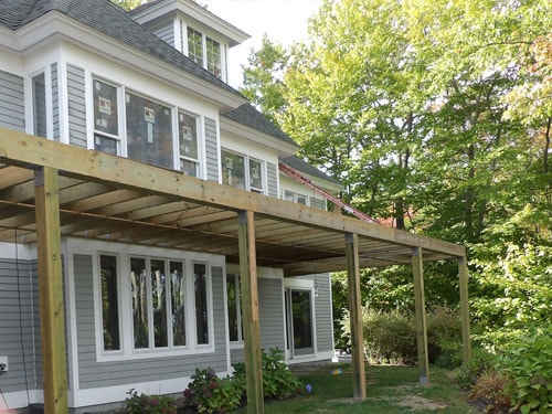 Large elevated deck structure with pressure-treated posts and beam framing on gray colonial home