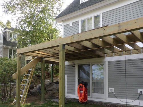 Under-deck view of elevated deck framing with pressure-treated posts, sliding door, and orange extension cord