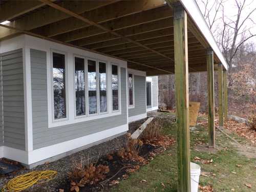 Under-deck view of completed elevated deck framing with posts and joists on gray home in late fall