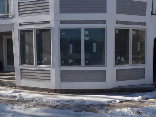 Close-up of new bay window installation with white trim and horizontal louvers on gray home exterior in winter
