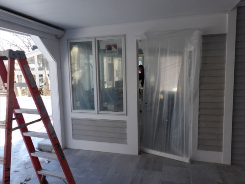 Screened porch conversion in progress with red ladder, new windows, and plastic sheeting over doorway in winter